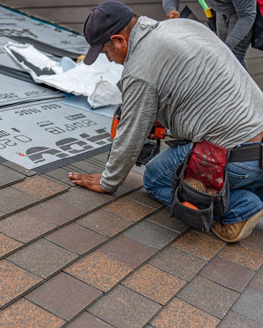 A roofer kneeling on a roof laying new shingles over underlayment