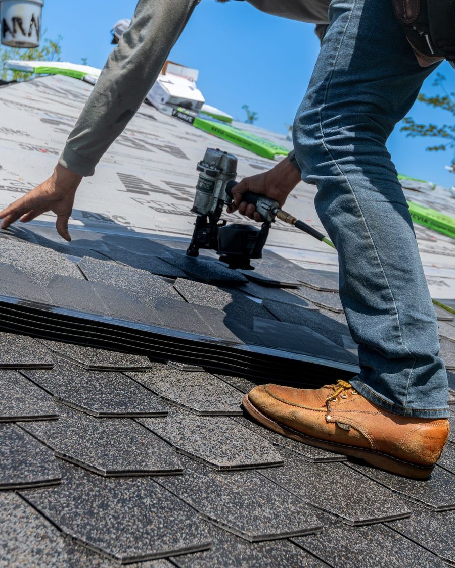 A roofer nailing new asphalt shingles onto a roof