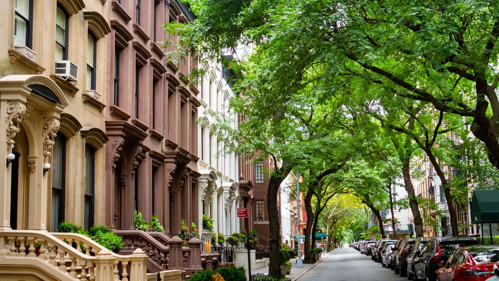 A tree lined street of brownstone homes in Brooklyn on a sunny day